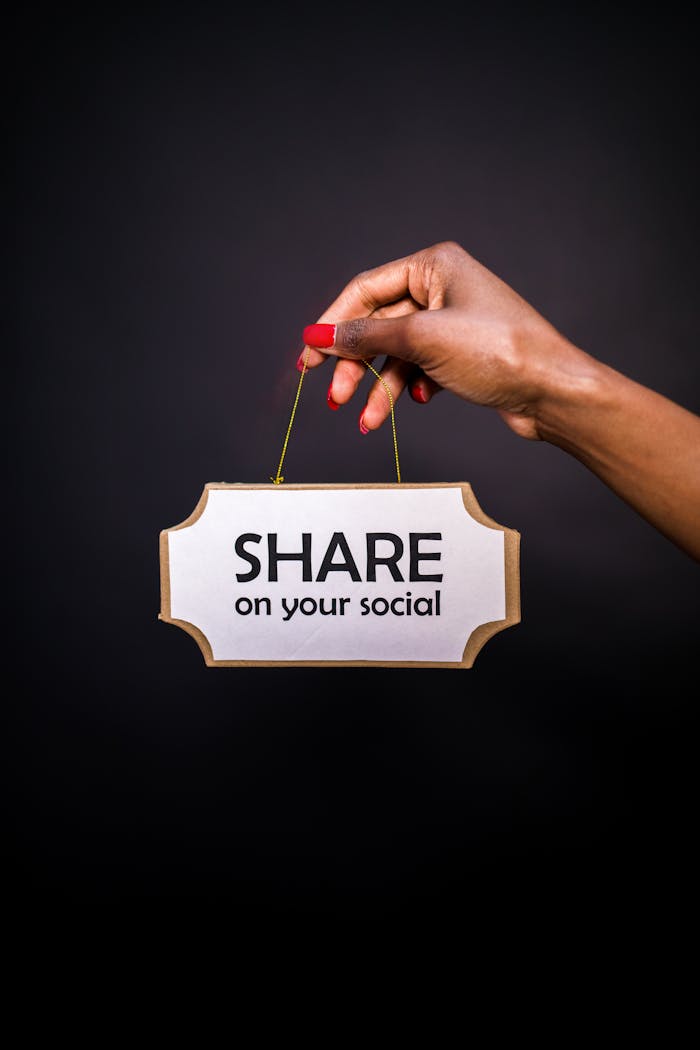 A hand holds a sign reading Share on your social against a dark background.